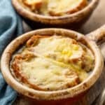 two bowls of french onion soup topped with toasted baguette and melted cheese