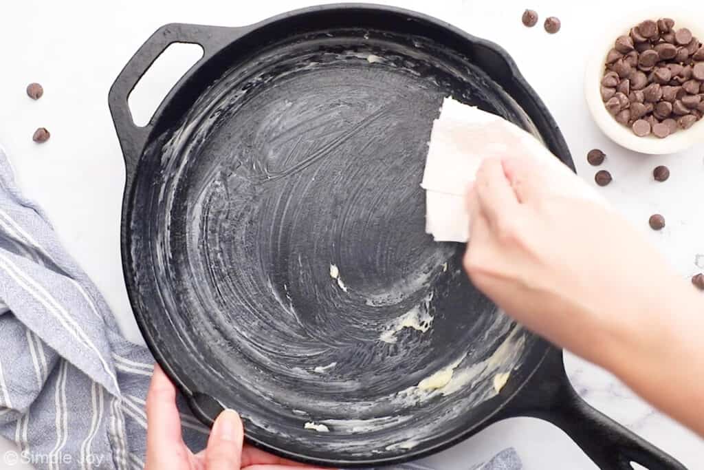 Overhead of person's hand rubbing butter in cast iron skillet to make pizookie recipe