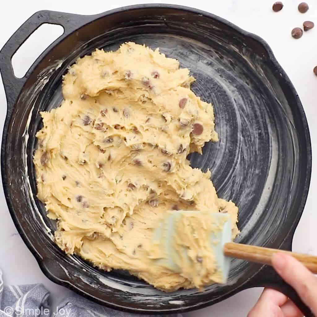 Overhead of rubber spatula spreading pizookie dough into a cast iron skillet