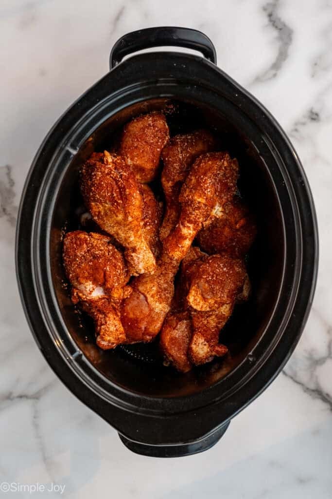 overhead of seasoned chicken drumsticks in slow cooker