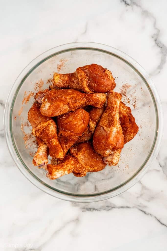 overhead of glass bowl of chicken drumsticks coated in chicken rub