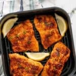 Pinterest graphic of air fryer salmon. Says "the best air fryer salmon simplejoy.com" Image shows overhead of air fryer basket of salmon with lemon wedges