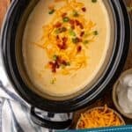 Pinterest graphic for crockpot potato soup. Image shows overhead of slow cooker of crockpot potato soup garnished with shredded cheese, diced bacon, and chives. Says "the best slow cooker potato soup simplejoy.com"