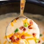 Pinterest graphic for crockpot potato soup. Says "slow cooker potato soup simplejoy.com" Image shows a ladle of potato soup with diced bacon, chives, and shredded cheese with slow cooker of soup sitting behind