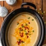 Pinterest graphic for potato soup recipe. Says "slow cooker potato soup simplejoy.com" Image shows overhead of slow cooker of crockpot potato soup garnished with shredded cheese, diced bacon, and chives.