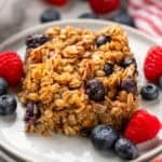 Piece of baked oatmeal on a plate with fresh blueberries and raspberries