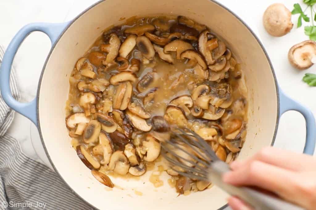 Overhead of soup pot of creamy chicken and wild rice soup ingredients with person's hand holding whisk