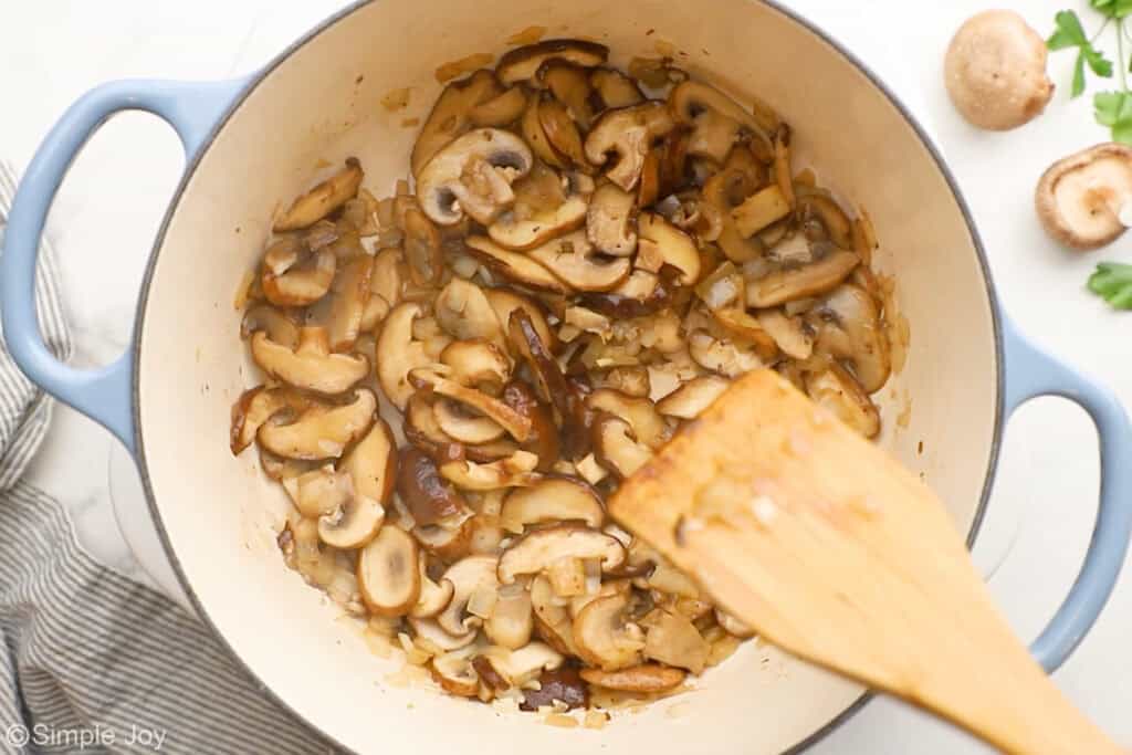 Overhead of soup pot of creamy chicken and wild rice soup ingredients with wooden spoon resting on pot