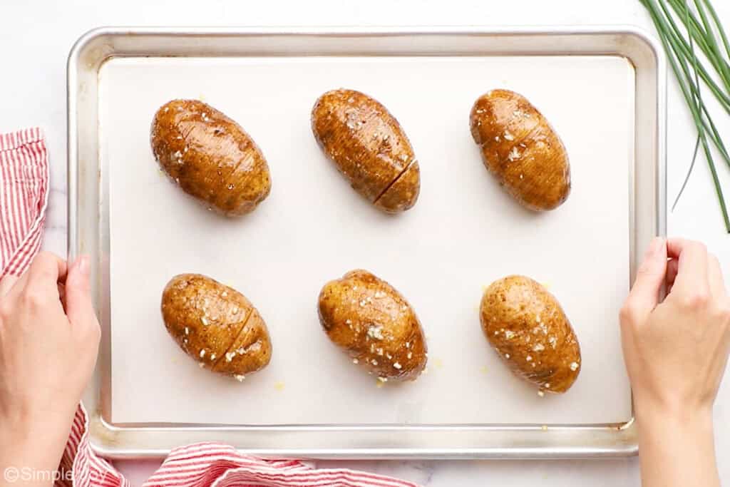Overhead of person's hands holding baking sheet of hasselback potatoes