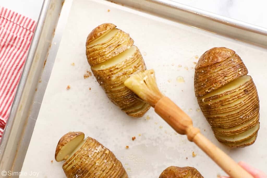Overhead of brush putting butter on hasselback potatoes on a baking sheet
