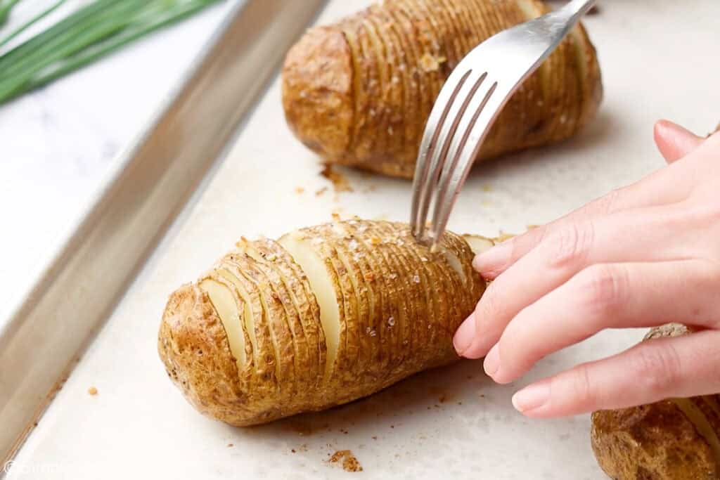 person holding hasselback potato with fork inserted into top of potato