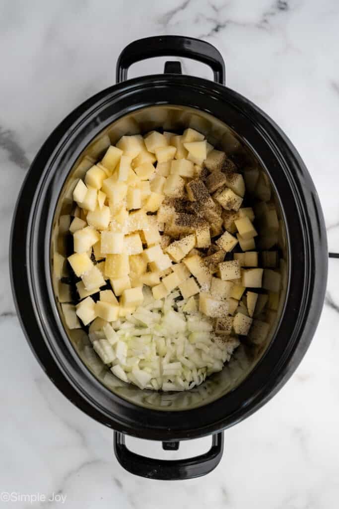 Overhead of a crockpot with diced potatoes, onions, and seasonings