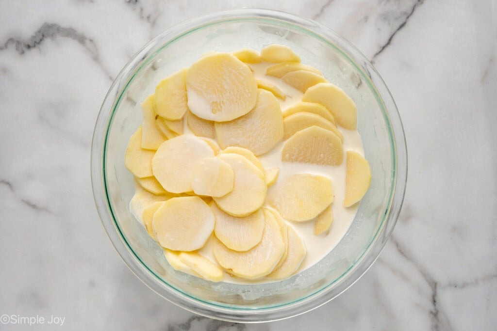 Overhead of bowl of thinly sliced potatoes in cream and chicken stock