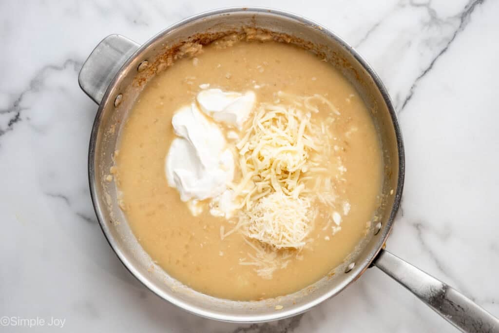 Overhead of skillet of with a creamy sauce, a scoop of sour cream, shredded mozzarella, and shredded parmesan