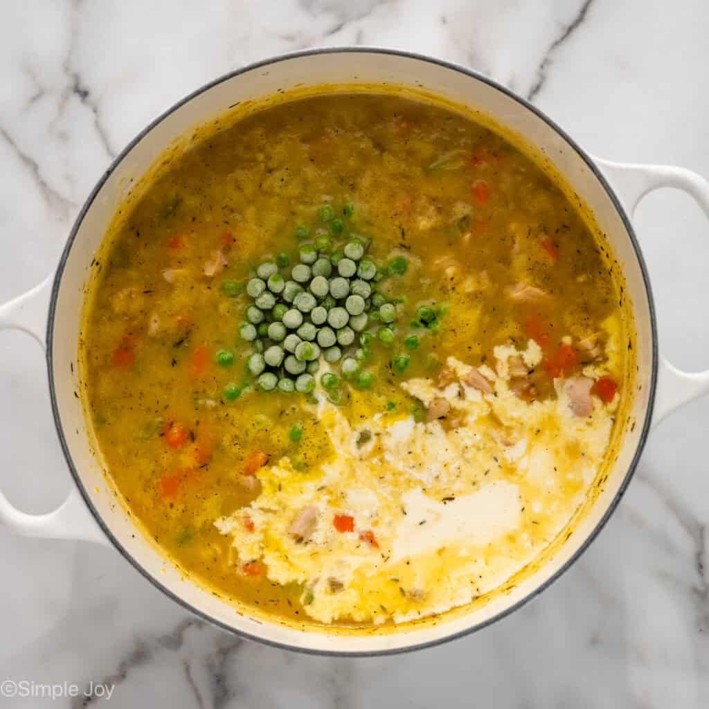 overhead of a dutch oven with soup, frozen peas just added, and heavy ceram