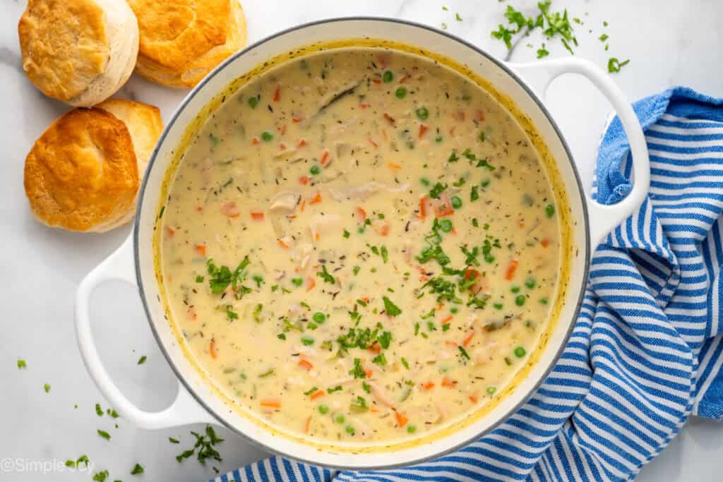 Overhead of pot of chicken pot pie soup with biscuits sitting beside
