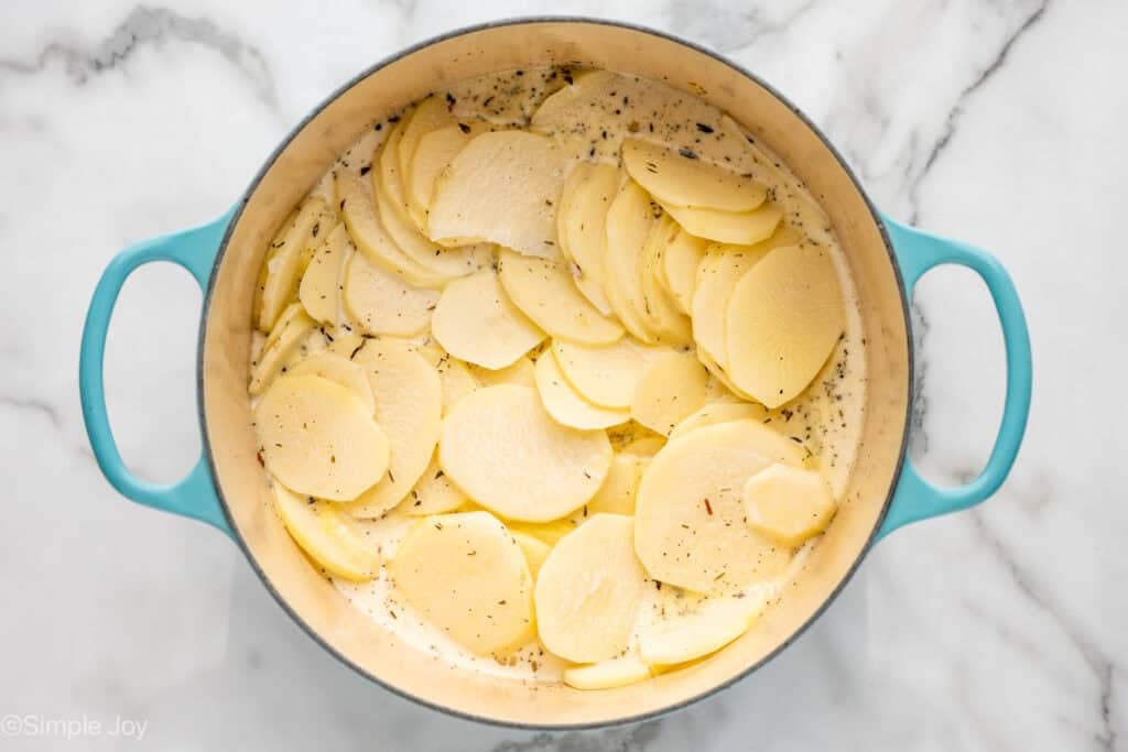 Overhead of pot of thinly sliced raw potatoes in a mixture of cream and spices