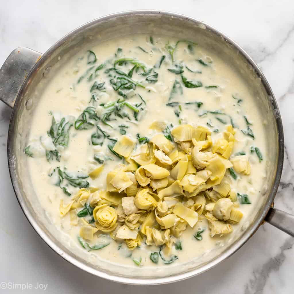 Overhead of skillet with creamy sauce, wilted spinach, and chopped artichokes