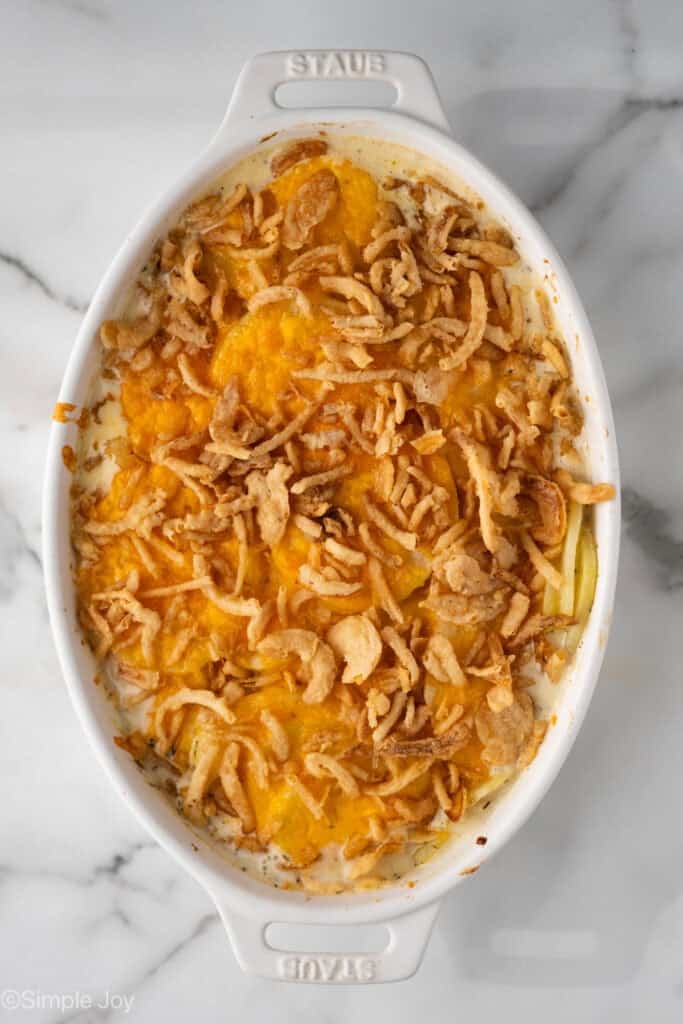 Overhead of baking dish with scalloped potatoes, topped with cheese and uncooked fried onions