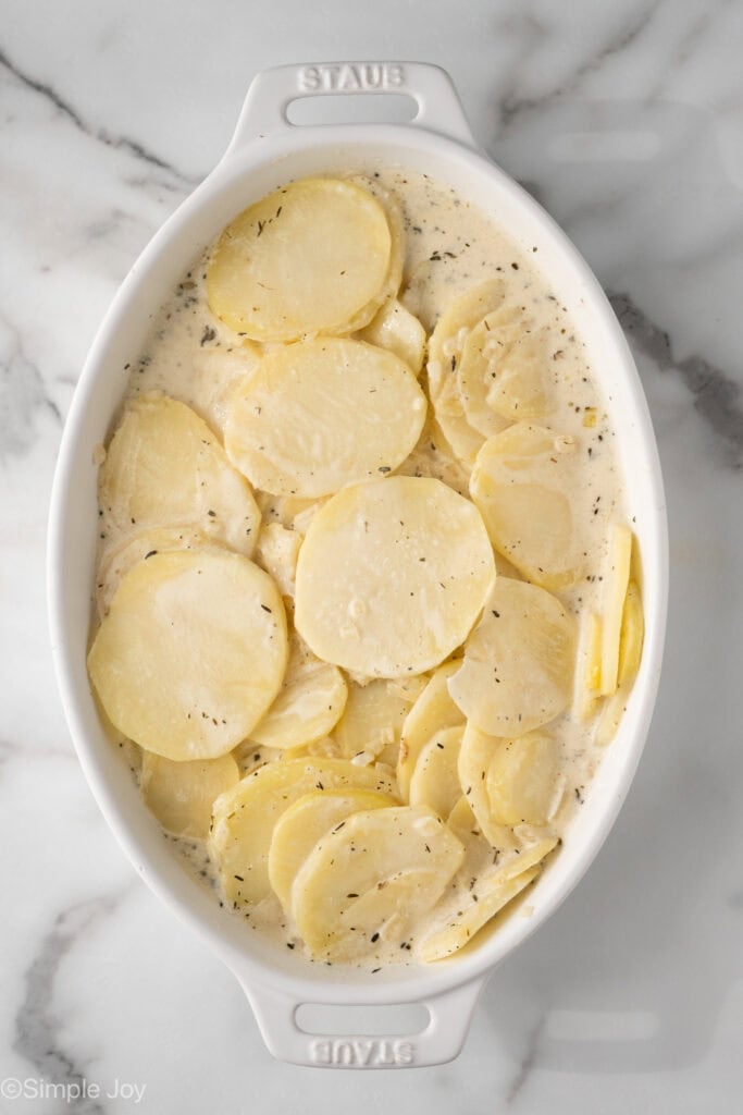 Overhead of baking dish with uncooked sliced potatoes for scalloped potatoes
