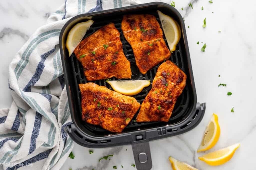 Overhead of air fryer basket of salmon and lemon wedges