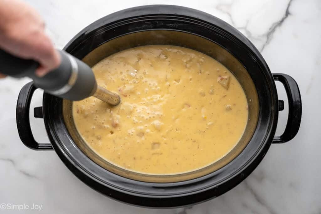 Overhead of immersion blender in a slow cooker of crockpot potato soup
