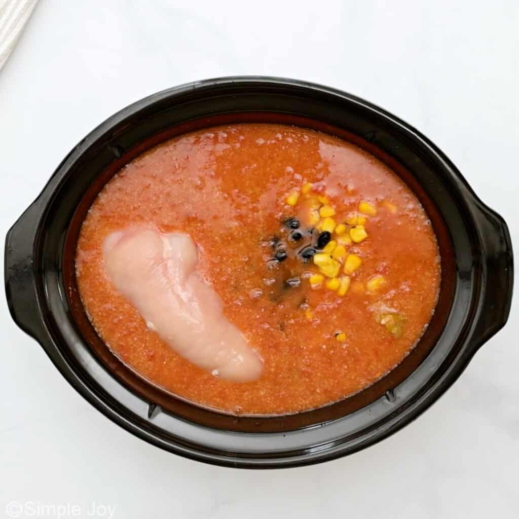Overhead of slow cooker of chicken enchilada soup with corn, black beans, and chicken breast