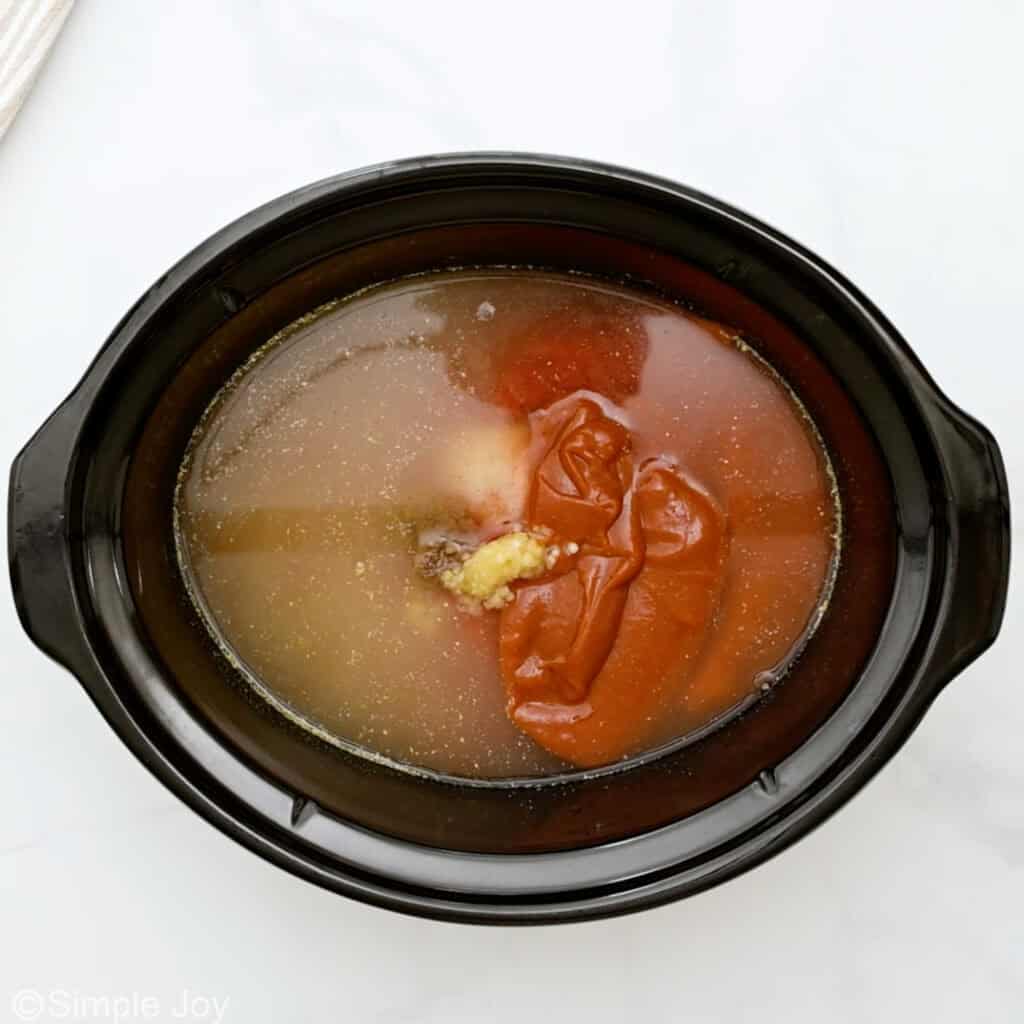 Overhead of slow cooker of chicken broth, tomato sauce, and garlic to make slow cooker chicken enchilada soup